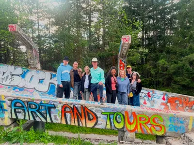 A tour group posing beside Art and Tours graffiti on the Olympic bobsled track